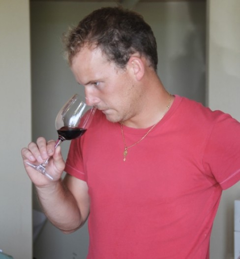 Homme en t-shirt rouge observant un verre de vin rouge en train de le humer