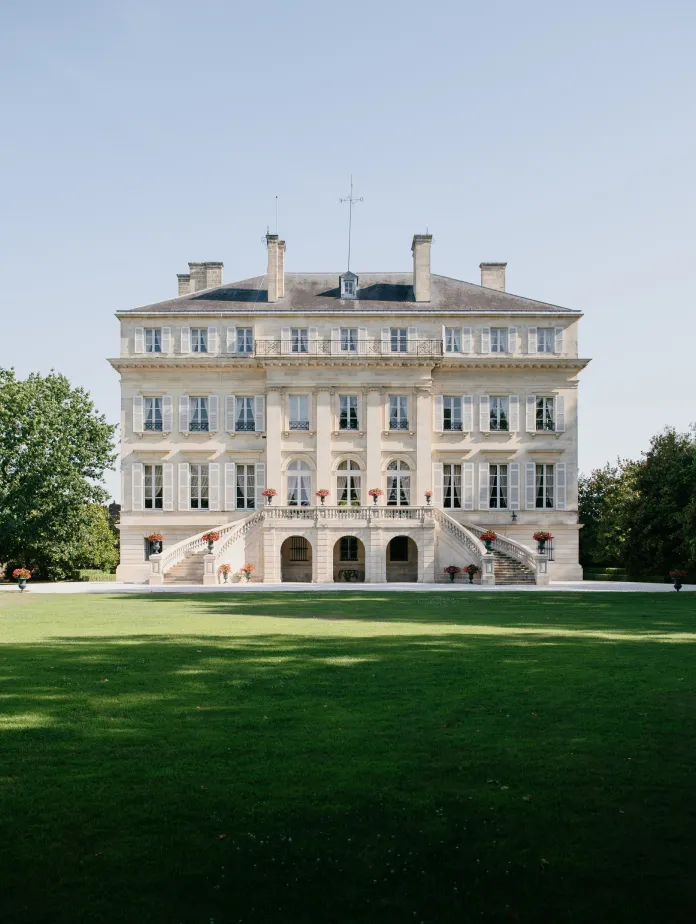 A grand, multi-storied building with a symmetrical façade, set on lush green grounds under a clear blue sky.
